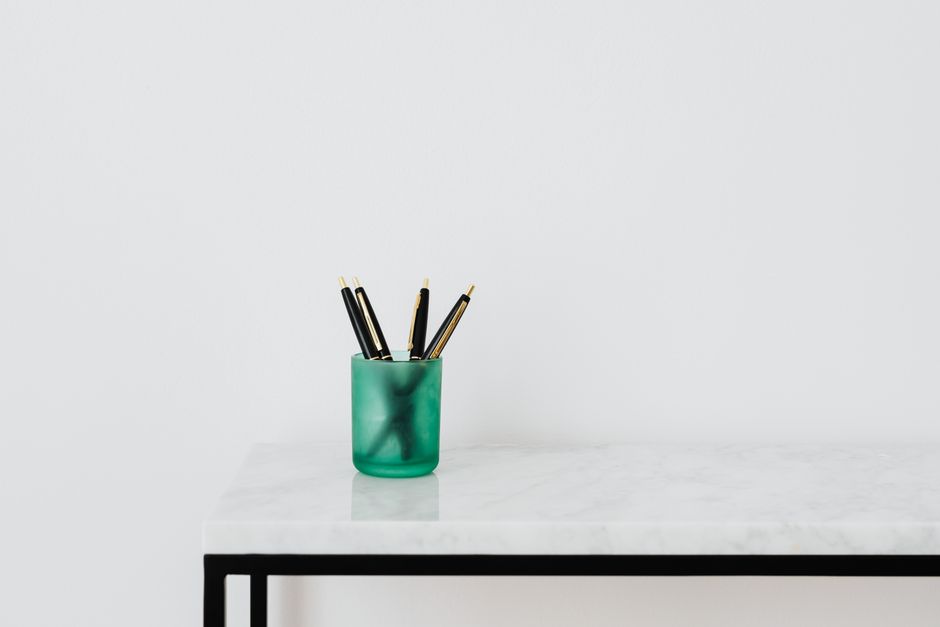 A minimalist workspace setup with a green pen holder on a white marble table against a white wall.